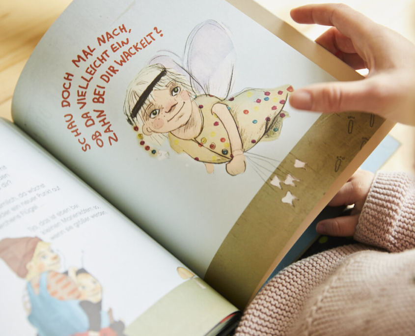 Eine gezeichnete Figur in einem bunten Bilderbuch, eine Frauenhand blättert die Seite um.